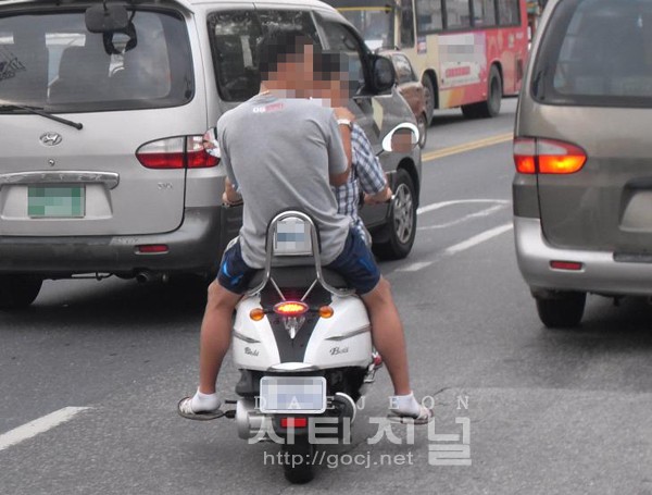 26일 많은 차들이 지나가는 도로 한 가운데, 충남 논산시 취암동에서 두 사람이 헬멧도 쓰지 않고 탑승해 위험하게 오토바이를 몰고 있다.
