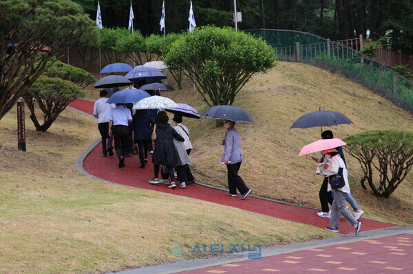[제67주년 현충일 추념식이 열린 천안보훈공원에 비가 내리는 가운데 시민들이 우산을 쓰고 헌화하러 이동하고 있다./현장 사진=유명조 기자]